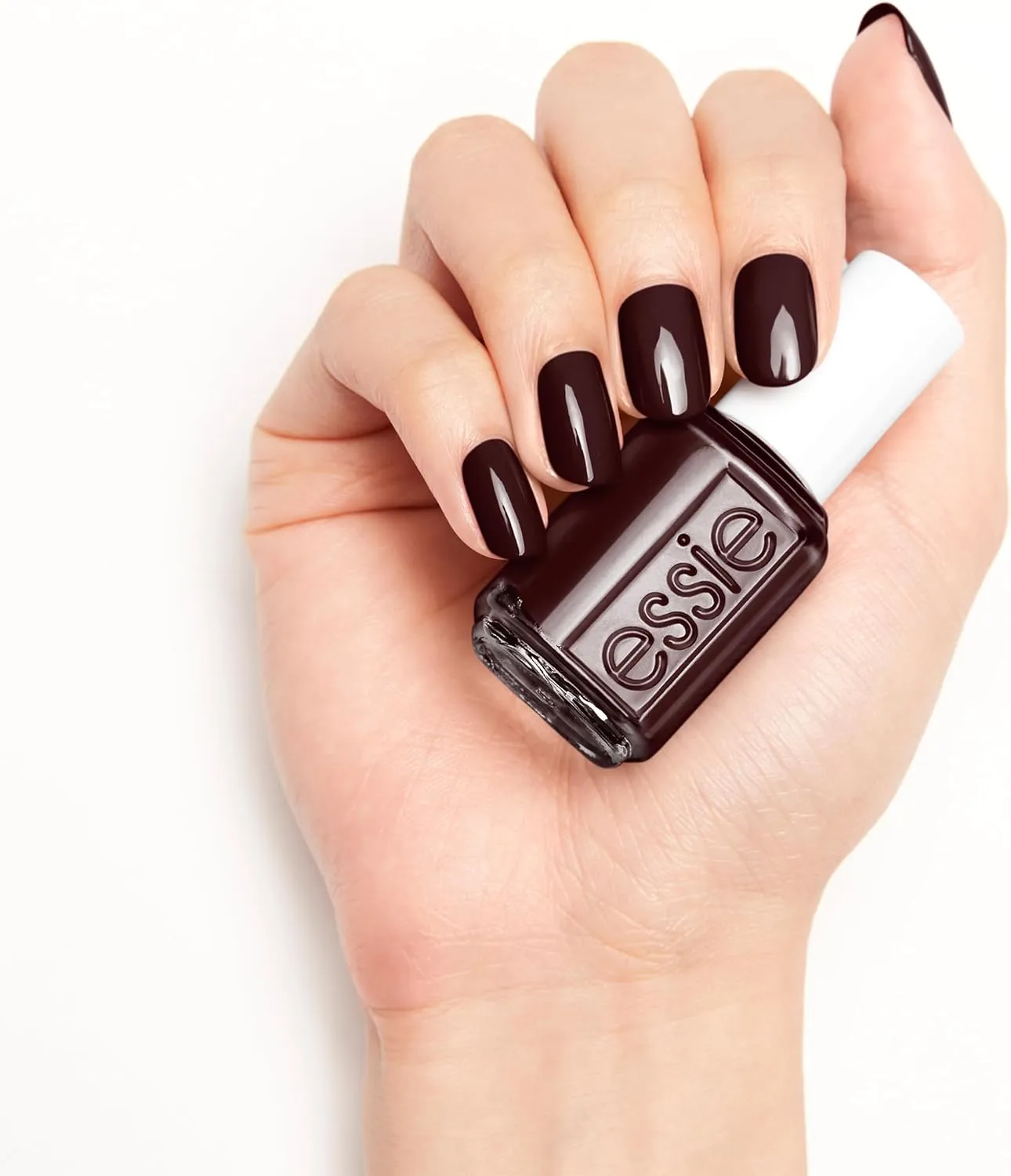 Mano con uñas rojo oscuro junto a un frasco Essie Wicked